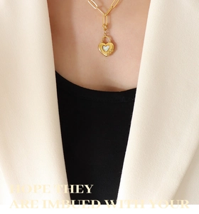 Gros plan d'un collier chaîne doré avec pendentif cœur et pierre aux reflets irisés