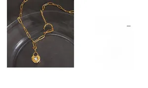 Détail d'un collier doré avec pendentif cœur et fermoir OT posé sur une assiette en verre