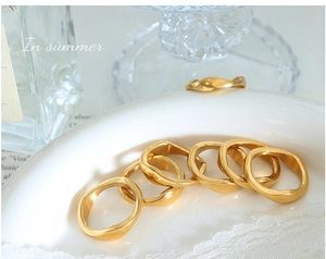 Close-up of irregular wave gold rings on a white porcelain tray with summer props