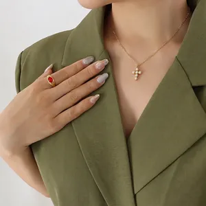 Collier croix en perles dorées et bague rubis sur mannequin en costume vert foncé