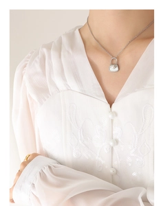 Détail d'un collier pendentif sac à main avec perle porté sur une chemise brodée blanche