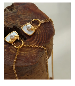 Détail d'un pendentif sac doré avec nacre blanche, perles et texture métallique matelassée