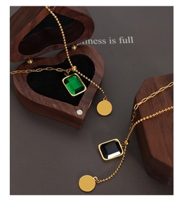 Détail d'un collier doré avec pendentifs en cristal émeraude et noir sur boîte en bois