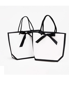 Detail of two white gift bags with black contrast edges and satin ribbon bows