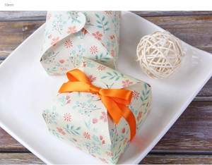 Detail einer floralen Geschenkbox mit orangefarbenem Polyesterband auf Holzgrund