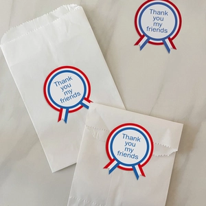 Trois autocollants cadeaux Thank You ronds avec rubans sur sacs en papier blanc sur marbre