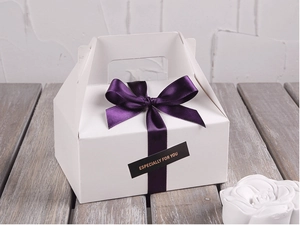 Detail einer weißen Geschenkbox mit dunkelvioletter Satinschleife und Gold-Siegel