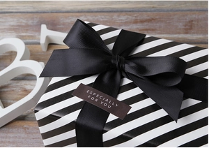 Detail of a black grosgrain ribbon bow on a striped gift box with a small hanging tag