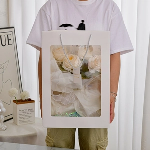 Handheld white window gift bag featuring champagne roses with white mesh wrap and silver handle