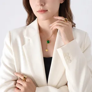 Collier doré élégant avec pendentif en cristal vert carré et franges sur blazer blanc