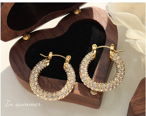Close-up of luxury U-shaped gold earrings with sparkling crystals in a wooden jewelry box