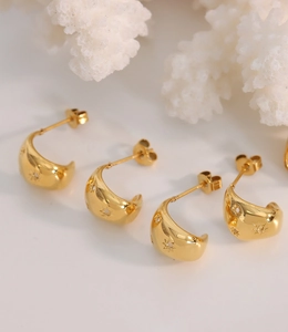 Détail de boucles d'oreilles créoles dorées avec gravures d'étoiles sur fond blanc pur