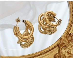 Macro detail of triple-layered gold-plated C-shaped hollow hoop earrings on vintage mirror