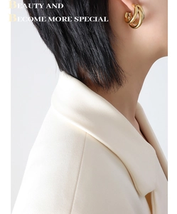 Close-up of triple-layered C-shaped gold hoop earrings on a model with beige blazer