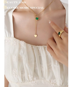 Detailed close-up of a heart emerald pendant necklace and matching gold ring on a model