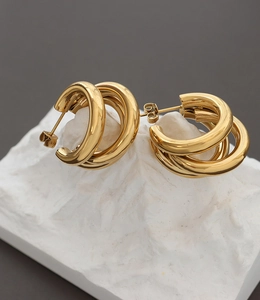 Close-up of triple-layered C-shape hollow tube gold earrings on white stone