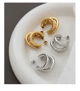 Detailed close-up of triple-layered gold and silver C-shaped chunky hoop earrings