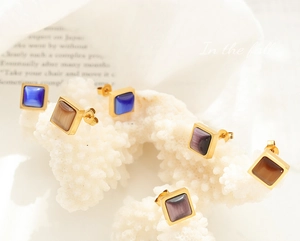Détail macro de boucles d'oreilles carrées en pierre œil de chat dorées sur corail blanc