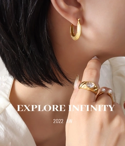 Gros plan d'une boucle d'oreille en C dorée 18K et d'une bague en perles sur un mannequin