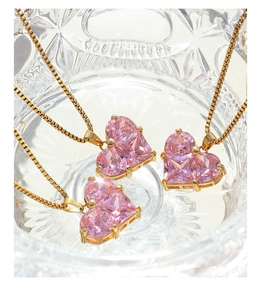 Makroaufnahme von drei rosa Herzanhängern mit Zirkonia und vergoldeten Ketten in Glas