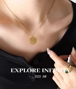 Nahaufnahme einer goldenen Kompass-Halskette und eines grünen Zirkonia-Rings