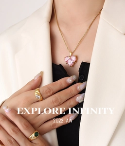 Nahaufnahme von herzförmiger rosa Edelsteinkette und goldenen Ringen an einem Modell