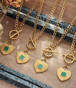 Detail of gold Cuban chain necklace featuring OT buckle and green heart pendant