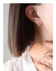 Close-up of a minimalist gold teardrop stud earring worn on a model's earlobe