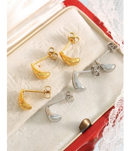 Close-up of minimalist gold and silver teardrop stud earrings in a vintage jewelry box