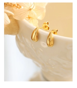 Detailed close-up of golden teardrop stud earrings hanging on a white ceramic bowl