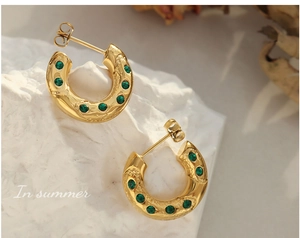 Détail de boucles d'oreilles C en or 18K avec texture martelée et zircons verts sertis