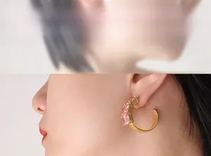 Close-up of gold C-shaped earrings with inlaid pink marquise gems worn by a model