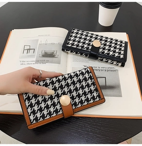 Détail du portefeuille pied-de-poule avec fermoir doré sur une table en bois chic