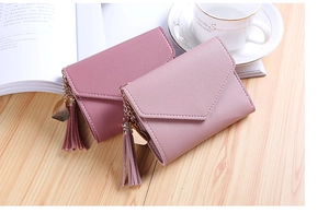 Close-up of pink mini wallets with leather tassels and gold heart pendants on wood desk