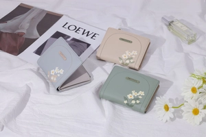 Tre portafogli compatti in ecopelle con stampe a margherita in blu, beige e verde