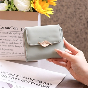 Detailed view of women's short wallet with metal leaf clasp and engraved brand logo
