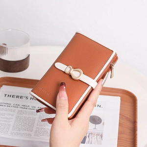 Detail of brown litchi grain leather wallet with golden bow and white trim