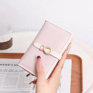 Light pink pebbled leather purse with golden bow clasp held against wooden tray
