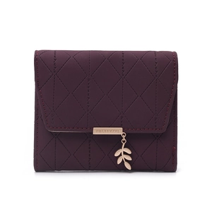 Close-up of quilted burgundy leather wallet featuring a gold leaf pendant and metal trim
