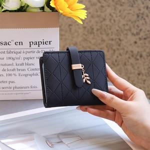 Detail of black quilted leather card holder featuring a gold leaf charm and buckle strap