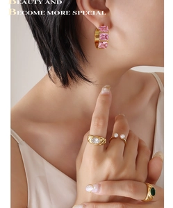 Detail of gold C-hoop earrings with pink rhinestones and assorted fashion rings