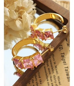 Macro shot of gold C-shaped earrings with square pink zircons on a vintage mirror