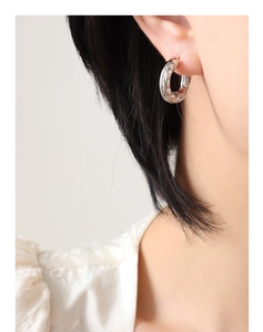Gros plan sur des boucles d'oreilles créoles C argentées avec texture et cristaux