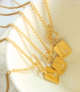 Macro shot of 18K gold plated OT buckle necklace with sailboat engraved square pendant