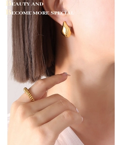 Détails de boucles d'oreilles dorées en forme de goutte et bague torsadée sur un modèle