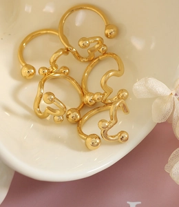 Close-up of golden wavy open rings with round beads on a ceramic plate with dried petals