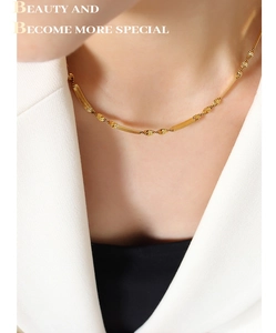 Detail of gold-plated geometric blade chain necklace layered on a white suit jacket