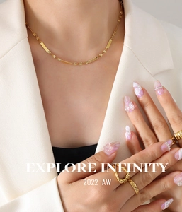 Close-up of golden blade chain necklace and textured rings worn with a white blazer