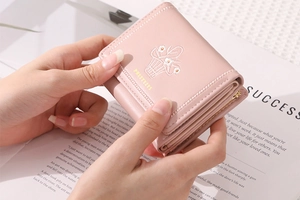 Pink PU leather trifold wallet with floral embroidery and gold logo held in hands