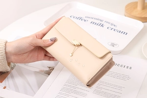 Detail of beige faux leather wallet featuring a gold heart pendant and zip pocket